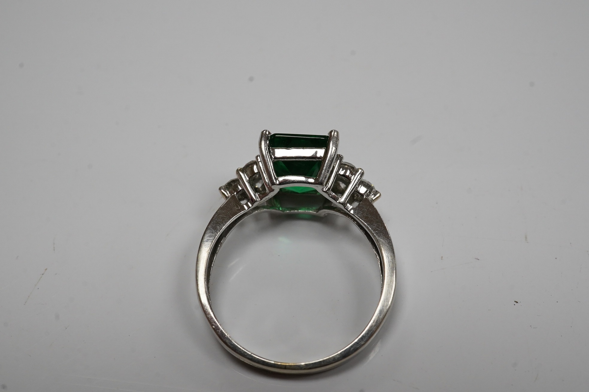 A modern 14k white metal and single stone green paste set dress ring, with six stone diamond set shoulders, size O, gross weight 3.6 grams. Condition - fair